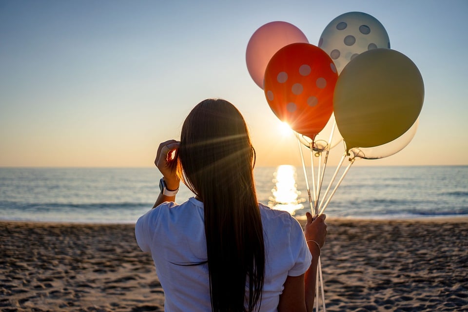 Menina segurando balões na praia