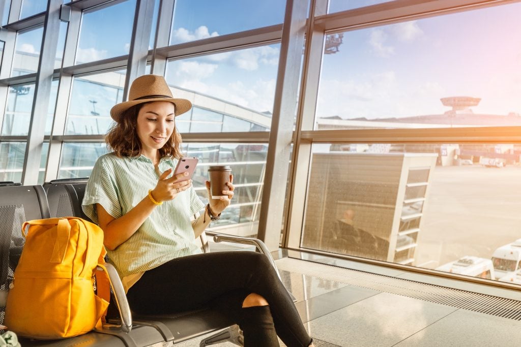 Mulher vendo celular no aeroporto e tomando café