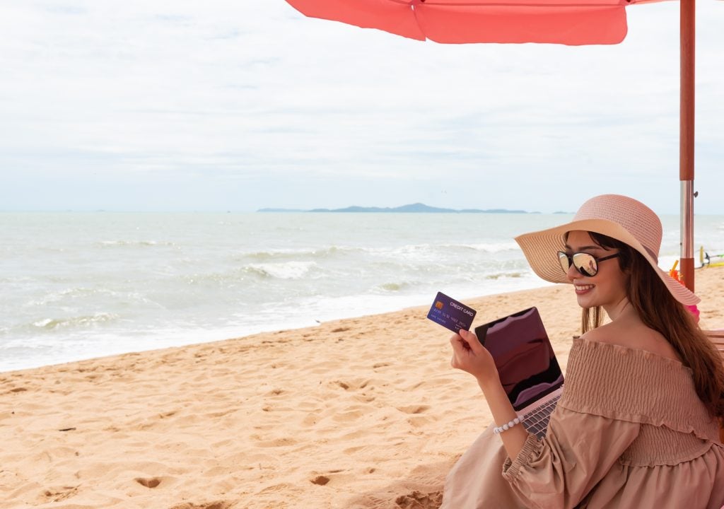 Mulher na praia segurando cartão de crédito