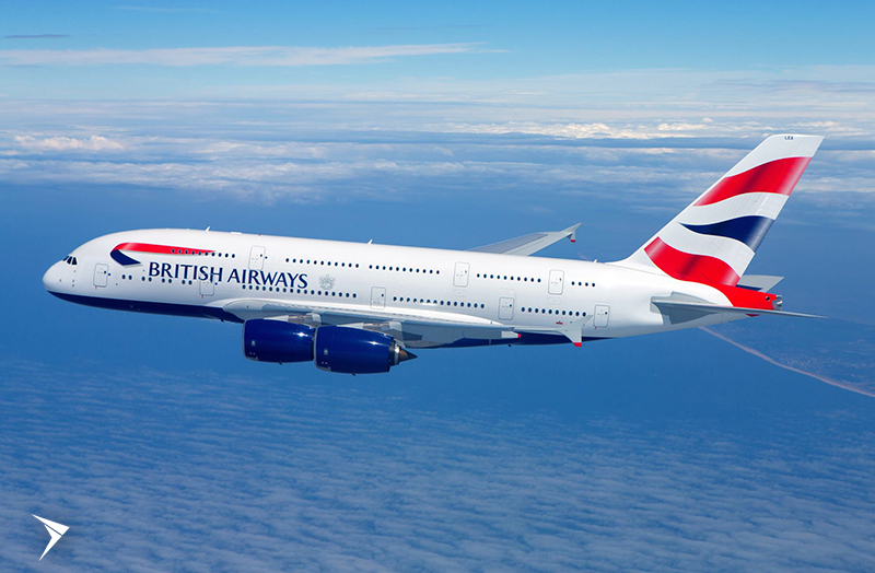 Um avião voando acima do oceano. O avião é branco e possui as cores vermelho e azul, na sua lateral está a logo da British Airways.